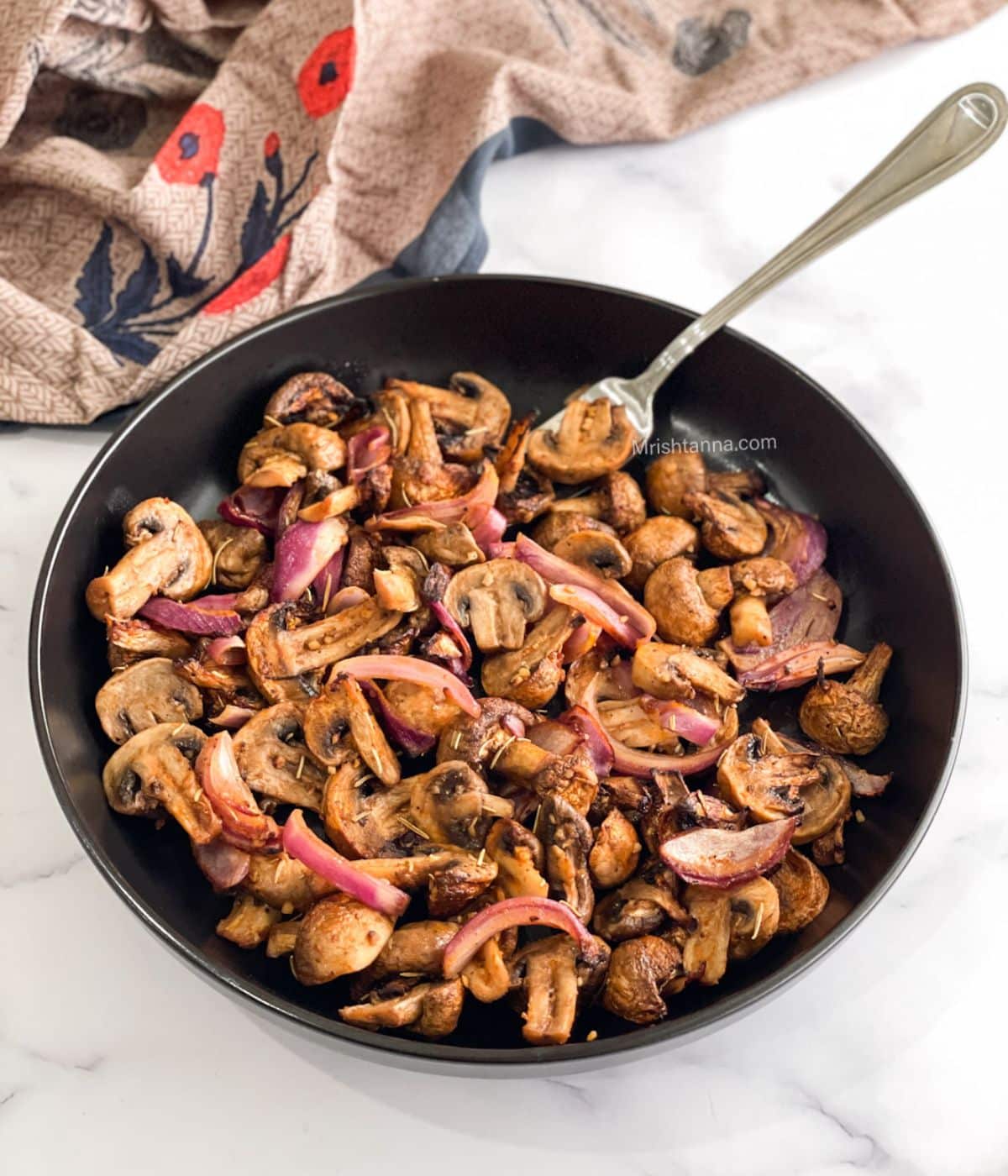 A plate of air fryer mushrooms and onions on the table with a fork inserted.