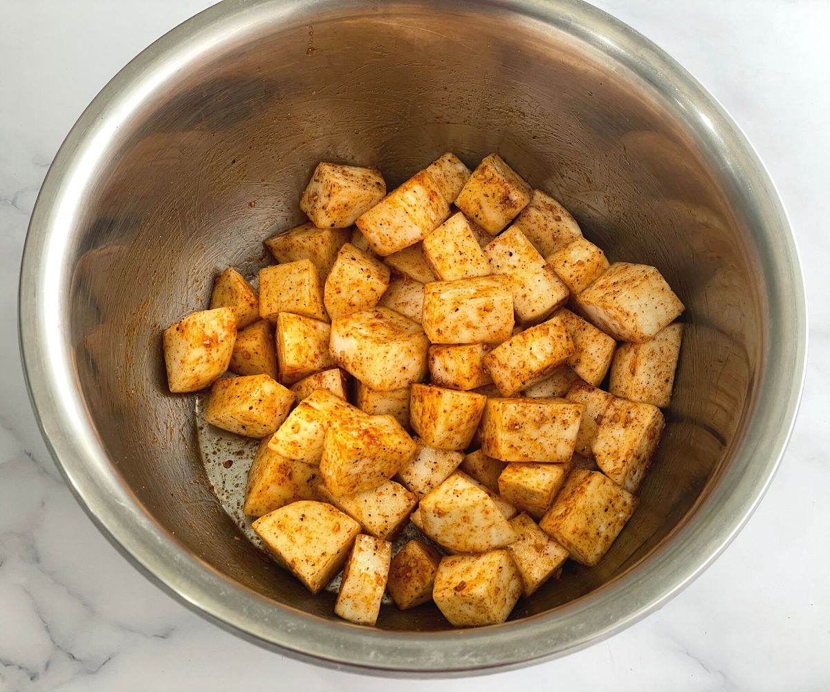 A bowl of turnips is coated with seasonings.