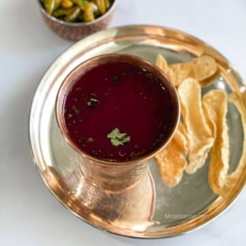 A cup of beetroot rasam is on the silver plate with fried chips.