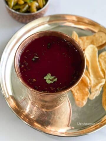 A cup of beetroot rasam is on the silver plate with fried chips.