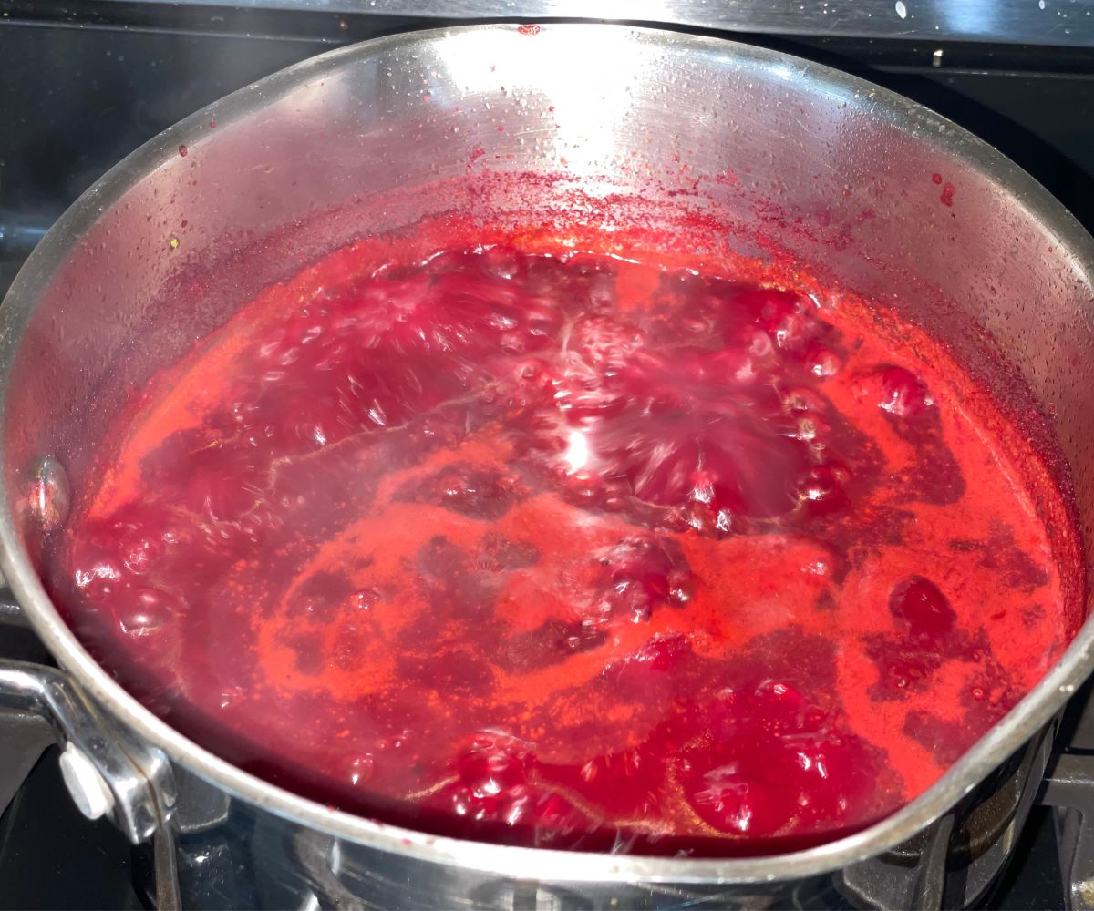 A pot is with boiling beetroot rasam over the stove top.