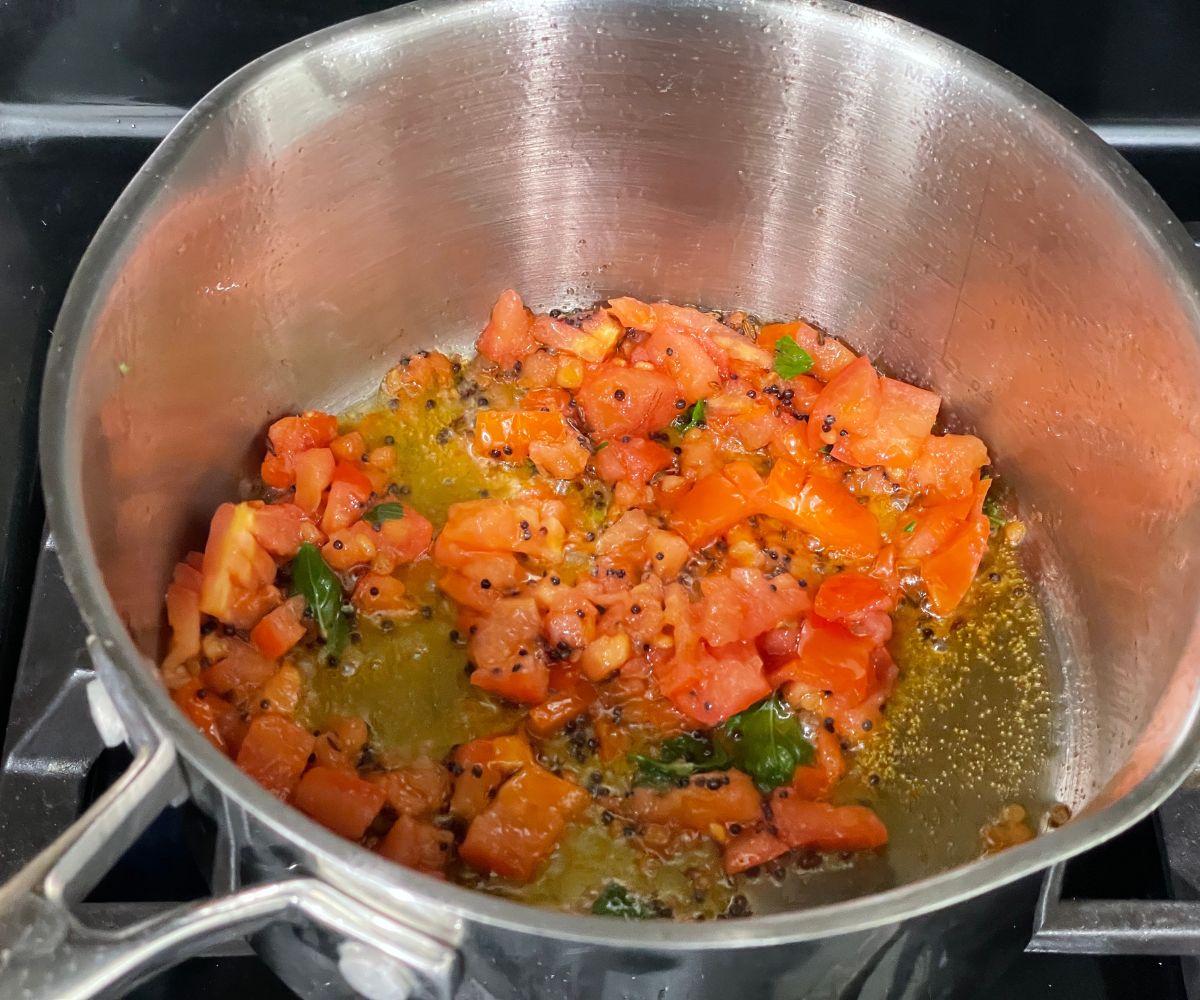 A pot is with spices, and chopped tomatoes over the heat.