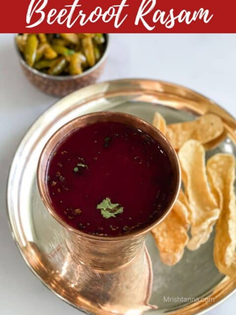 A mug of beet rasam is on the plate with chips.
