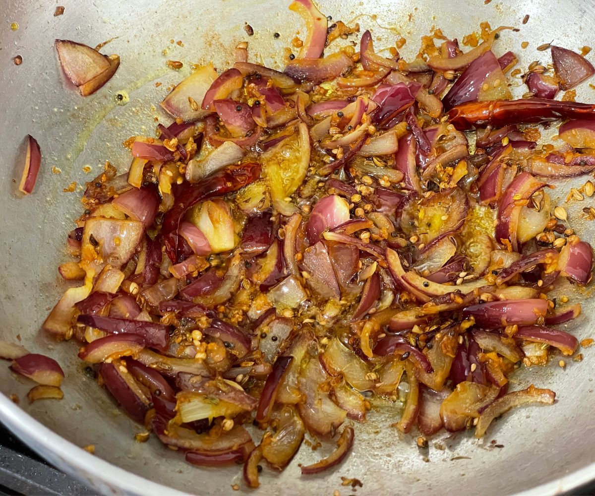 A pot is with sauteed onions and spices over the heat.