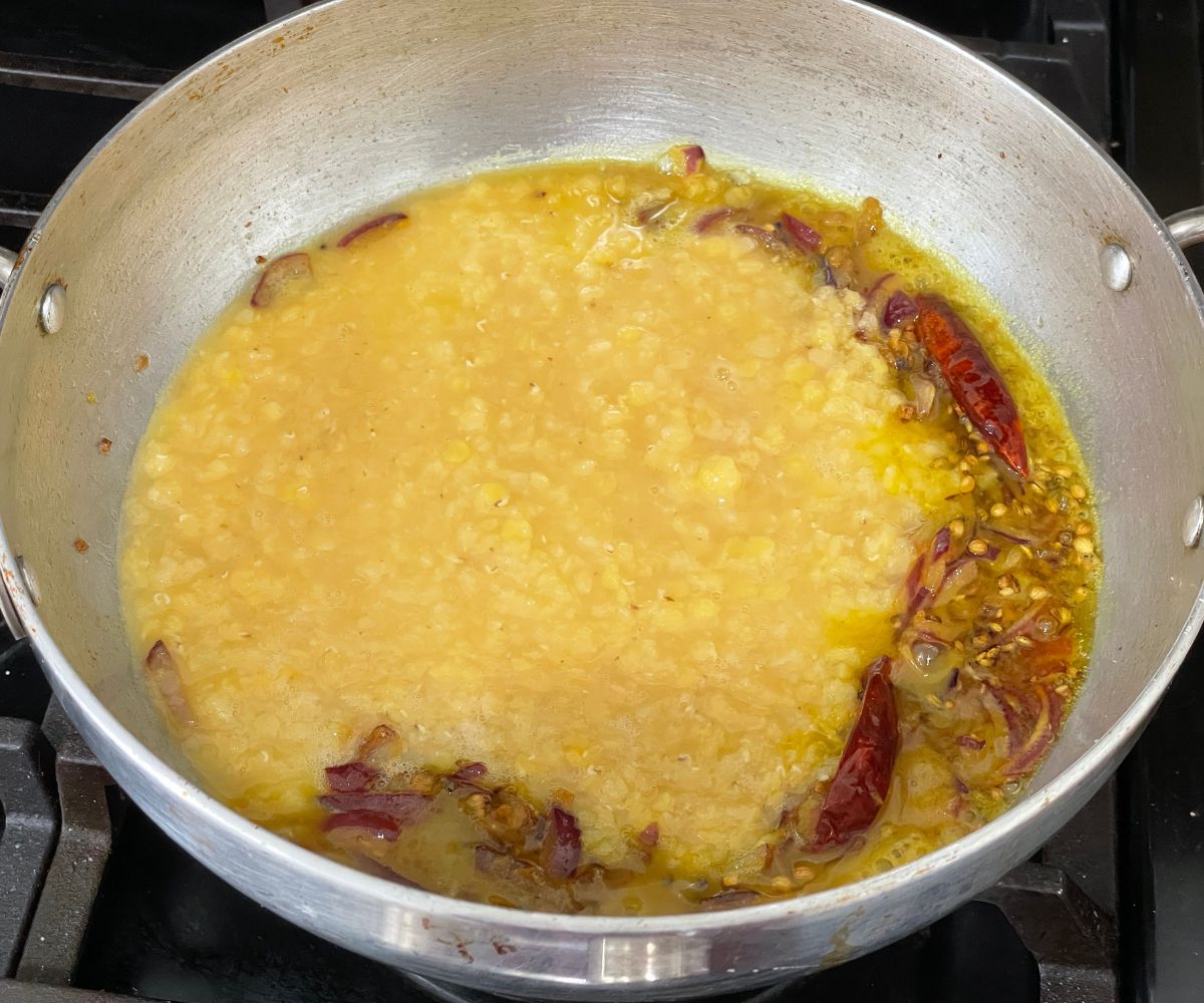 A pot is with spices and cooked red lentils over the heat.