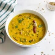 A bowl of Bengali masoor dal is on the table and topped with cilantro.