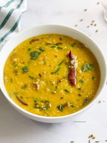 A bowl of Bengali masoor dal is on the table and topped with cilantro.