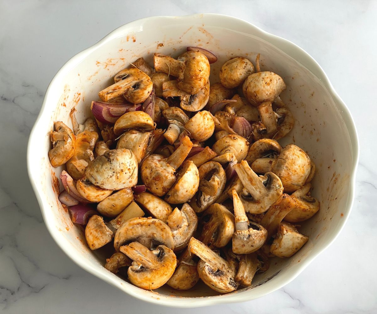 A bowl is filled with spices coated mushrooms and onions.