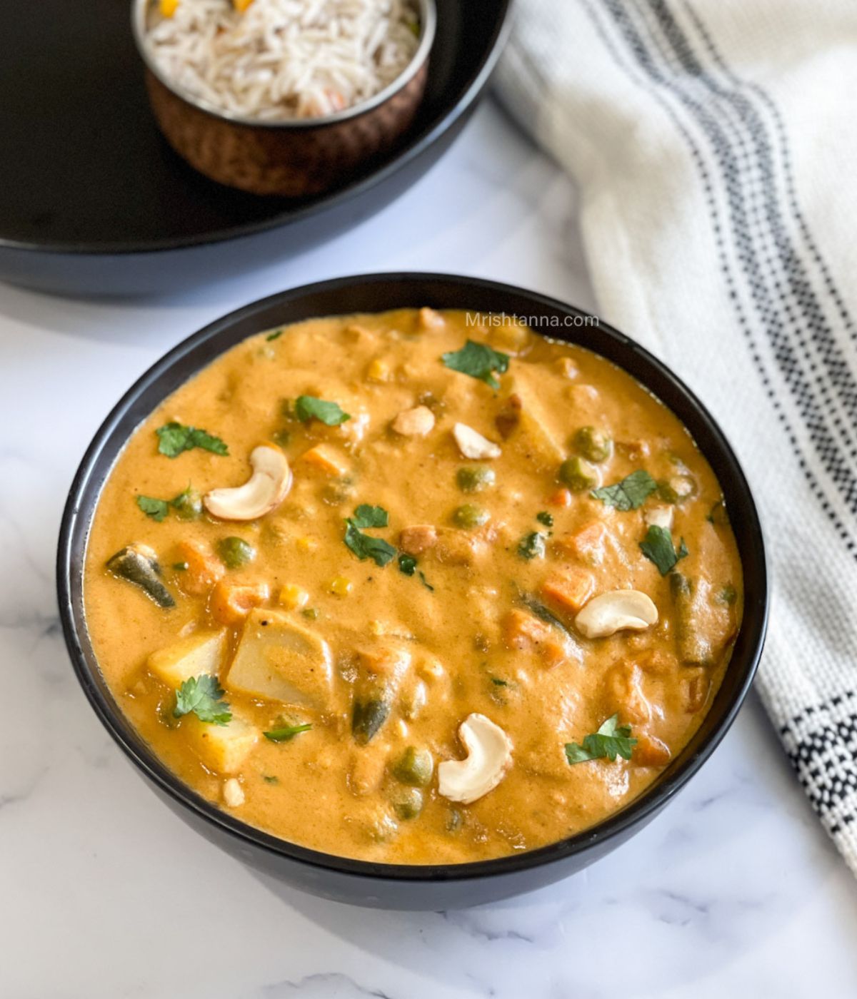 A black bowl is filled with vegetable korma on the table.