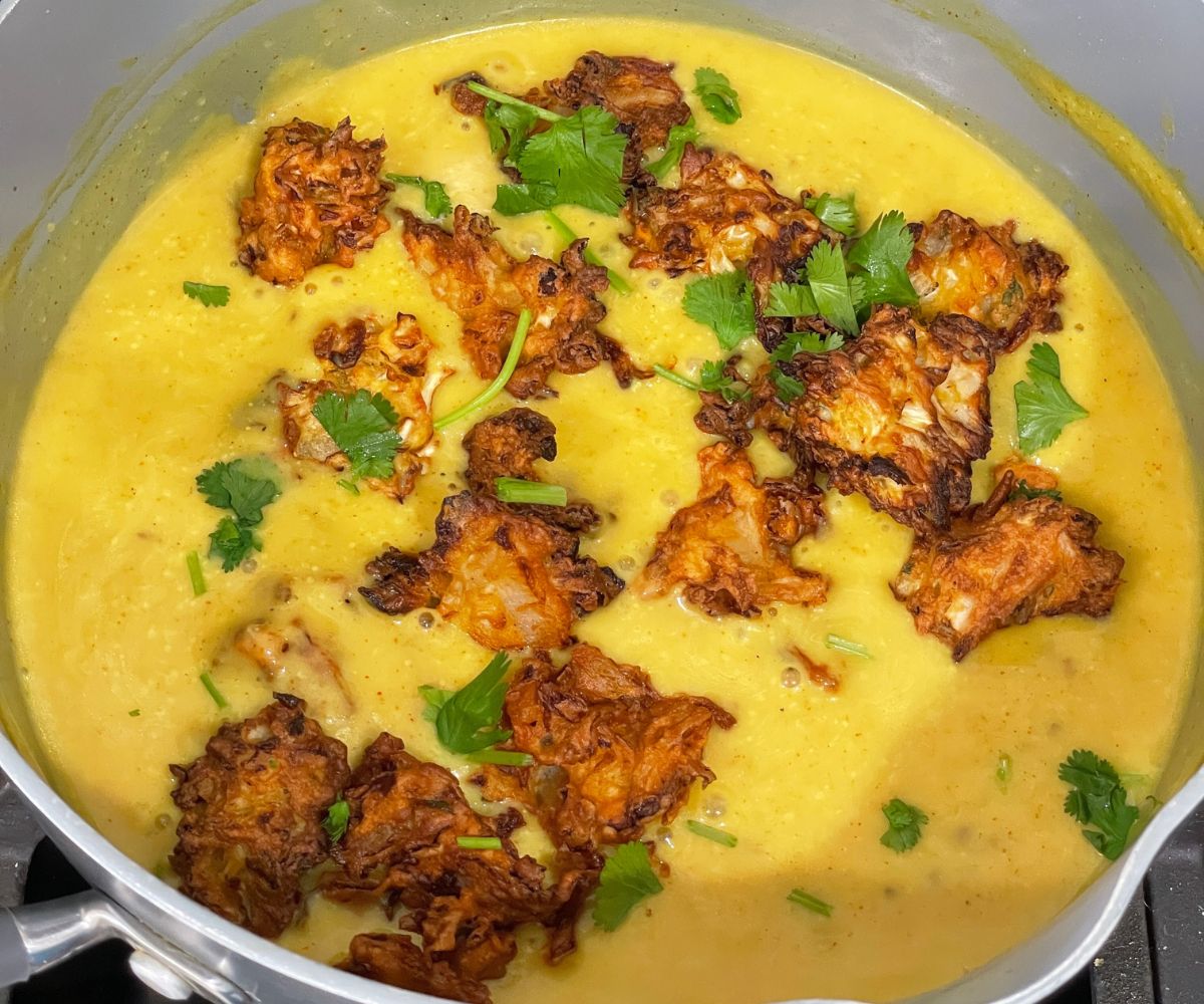 A pot is with kadhi pakora curry over the stove top.