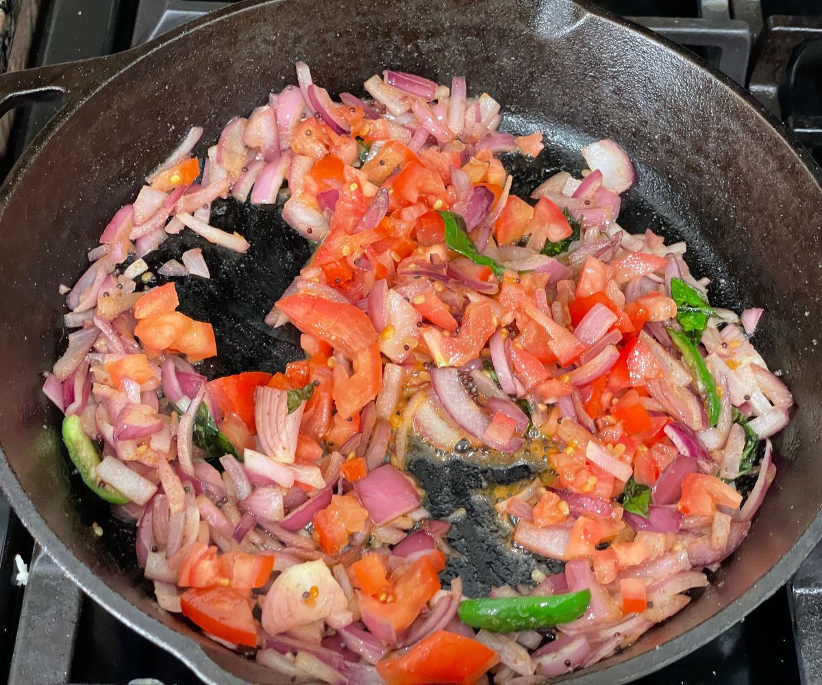 Cast iron pan is with chopped onions and tomatoes over the heat.