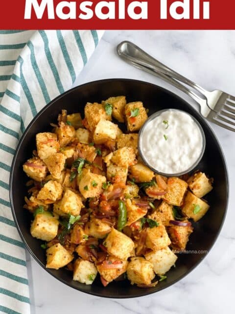 A plate is filled with masala idli and bowl of curd placed by the cloth napkin and forks.