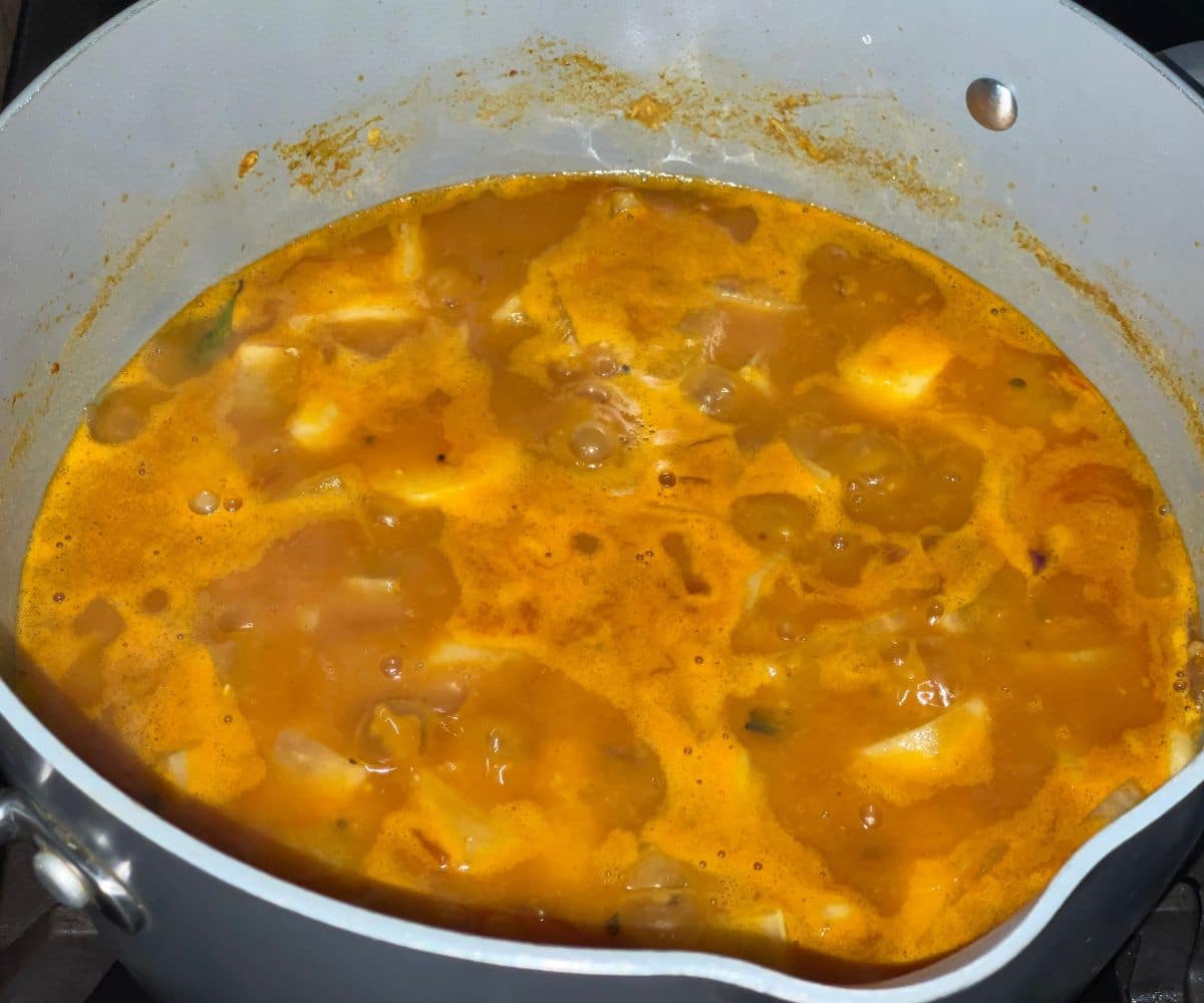 A pot is with boiling Mullangi sambar over the stove top.