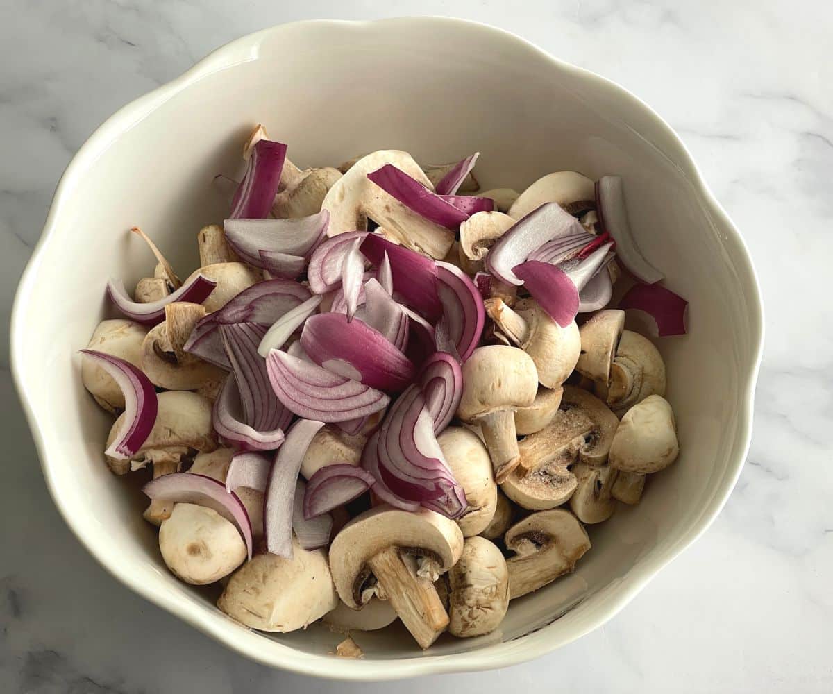 A bowl is with halved mushrooms and sliced onions.