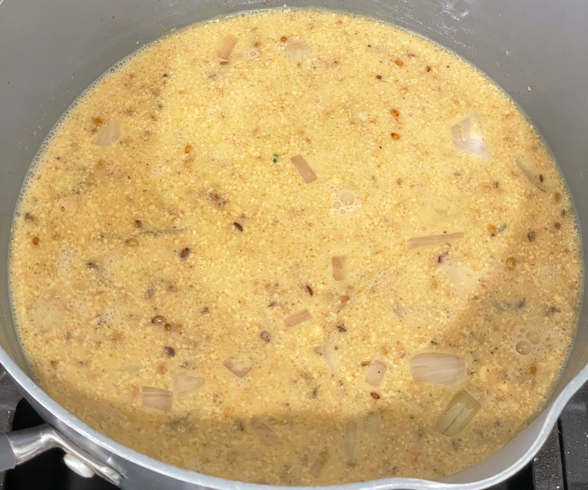 A pan is with kadhi mixture over the heat.