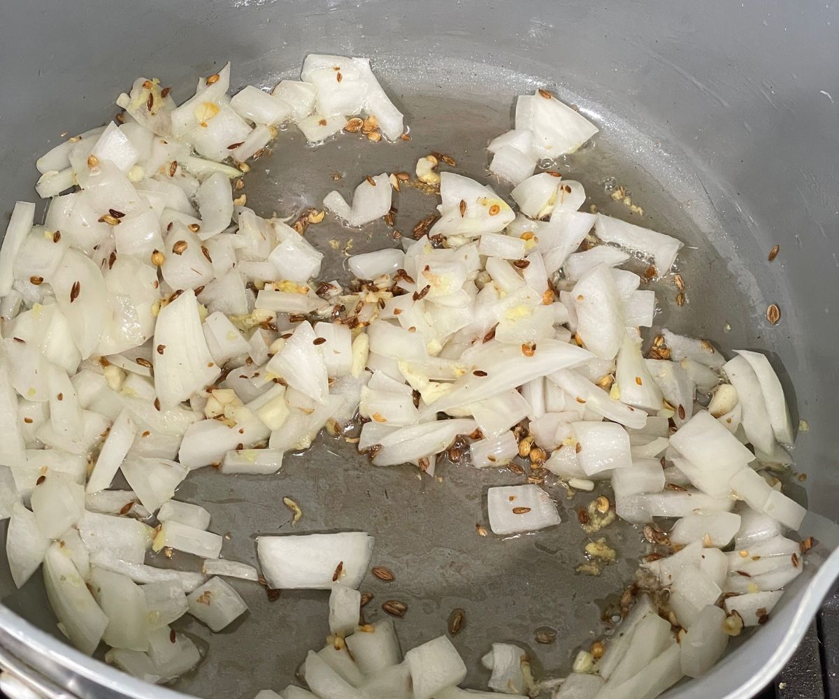 A pan is with oil, spices, and chopped onions over the heat.