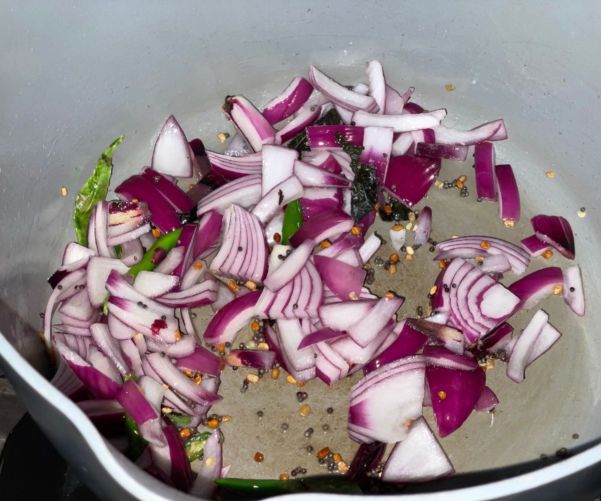 A pot is with oil, spices, amd chopped onions over the heat.