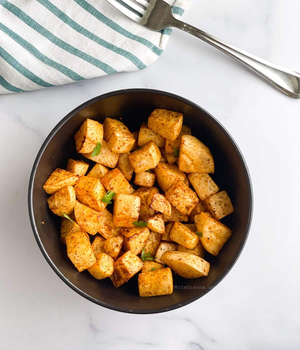 A bowl is with roasted turnips on the table along with a fork.