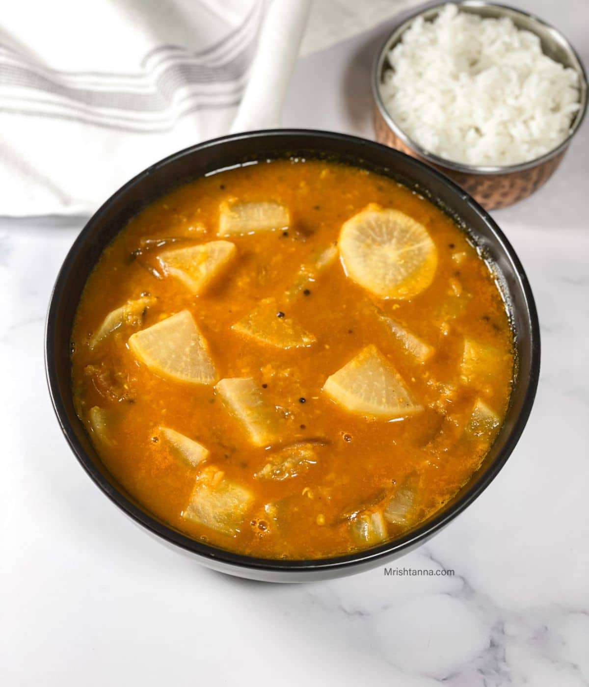 A bowl of radish sambar is on the table along with a bowl of rice.