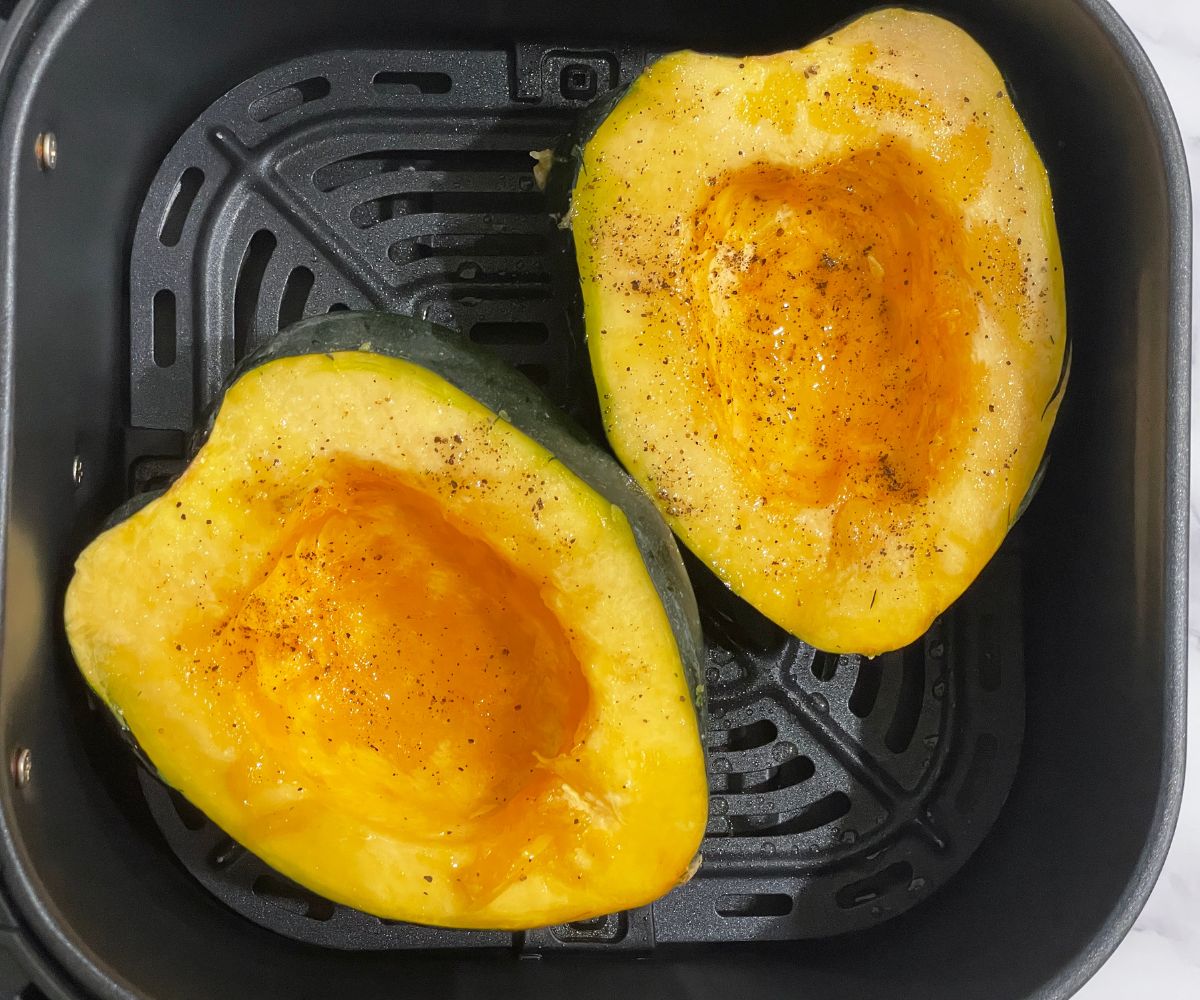 Halved acorn squash is inside the air fryer basket.