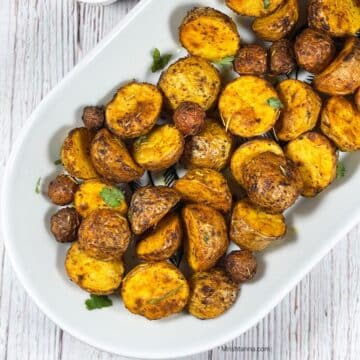 A ceramic tray is with roasted baby potatoes.