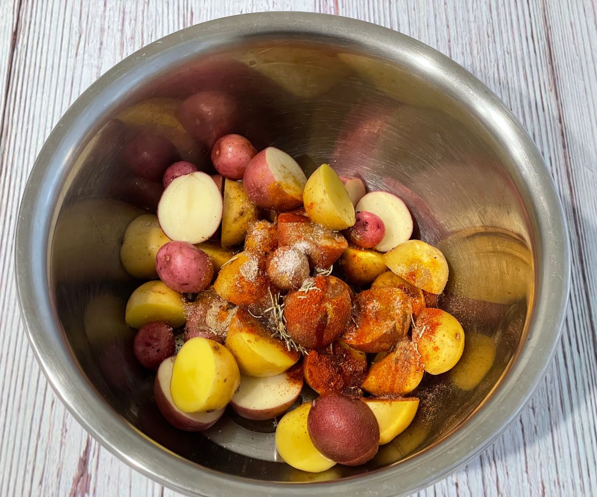 A bowl is with halved mini potatoes and seasonings.