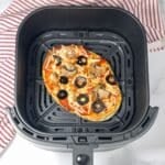 Air fryer basket is with vegan naan pizza.