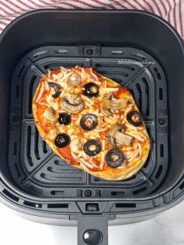 Air fryer basket is with vegan naan pizza.