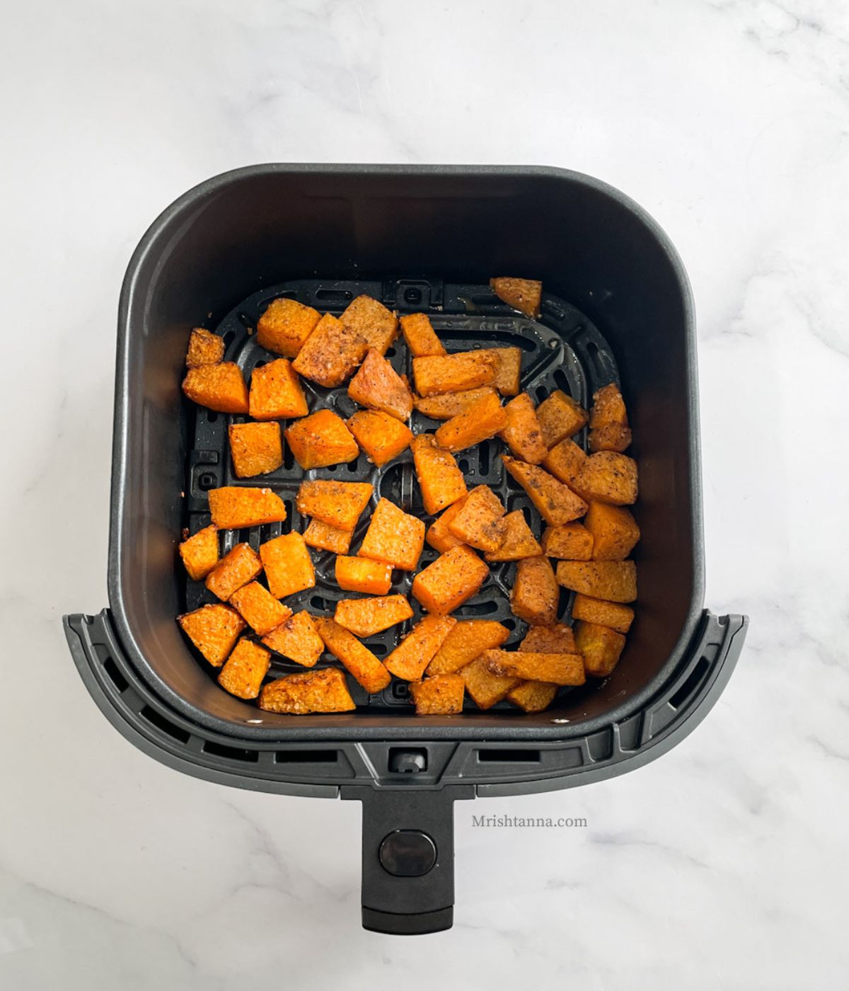 Air fryer basket is with roasted pumpkins.