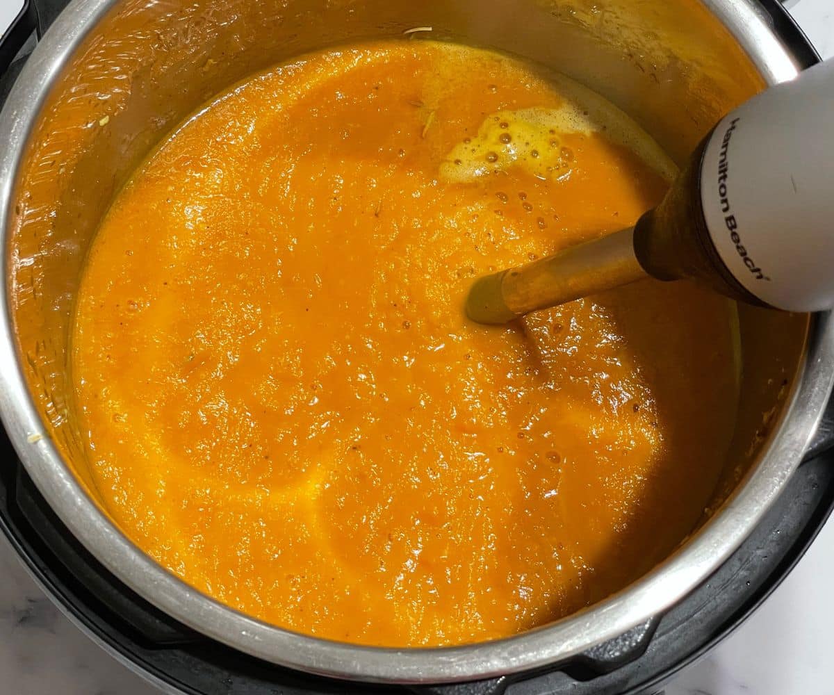 An instant pot is with butternut squash, carrot ginger soup is immersing with hand blender.