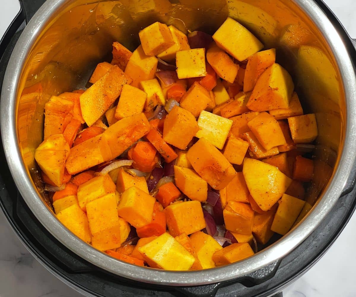An instant pot is with butternut squash, carrots and spices on saute mode.