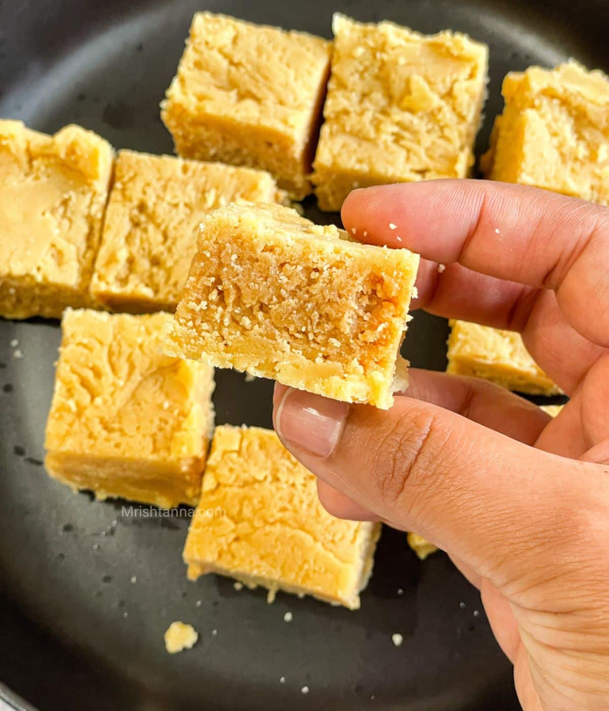 A hand is holding up a piece of vegan mysore pak.