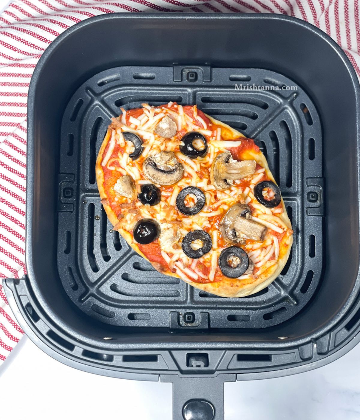 Air fryer basket is with vegan naan pizza.