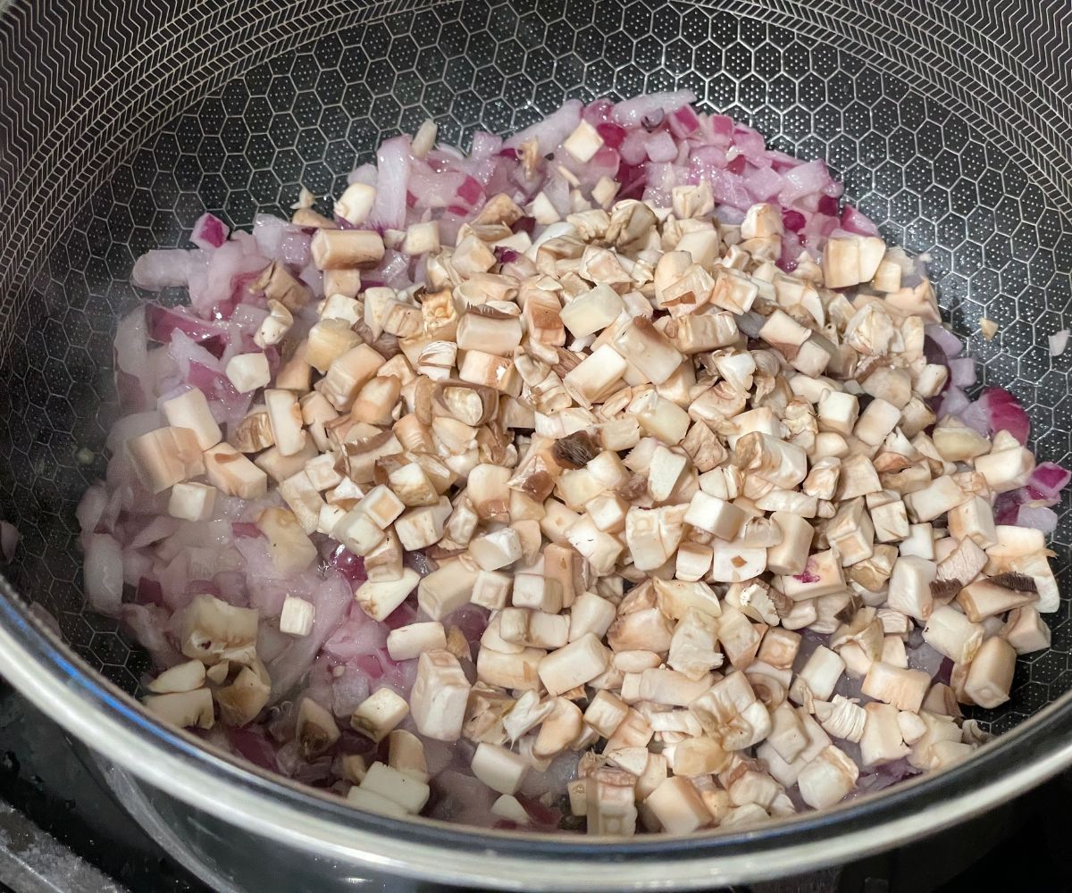A pan is with chopped onions, mushrooms over the medium heat.