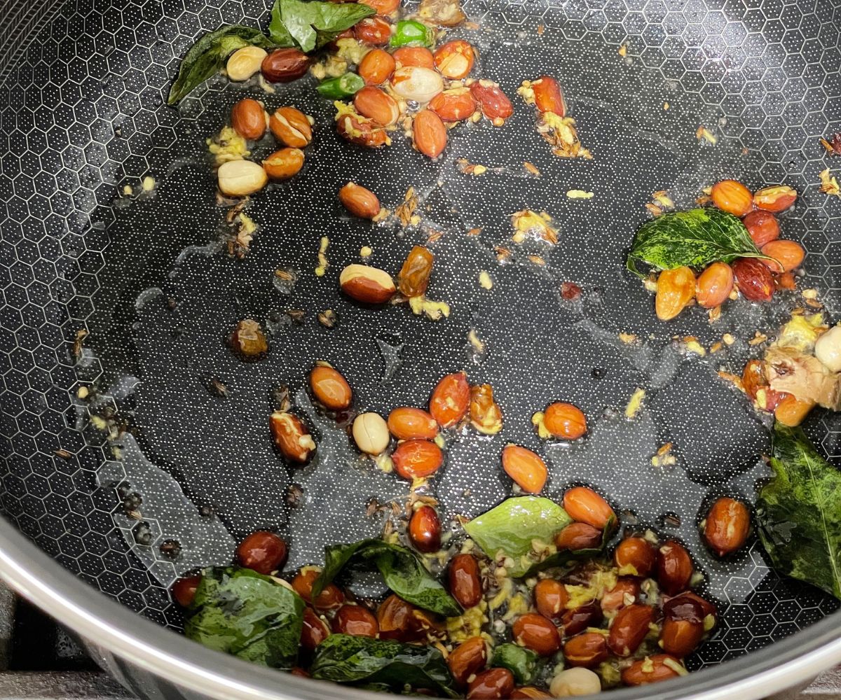 A pan is with oil, spices, and peanuts over the heat.