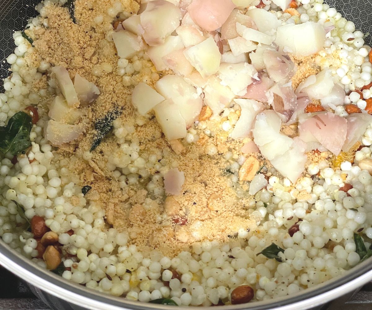 A pan is with sabudana khichdi and topped with potatoes and peanuts.