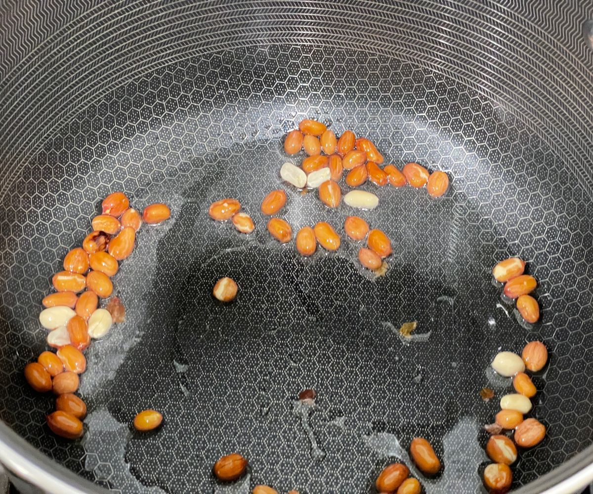 A non stick pan is with oil and peanuts over the heat.