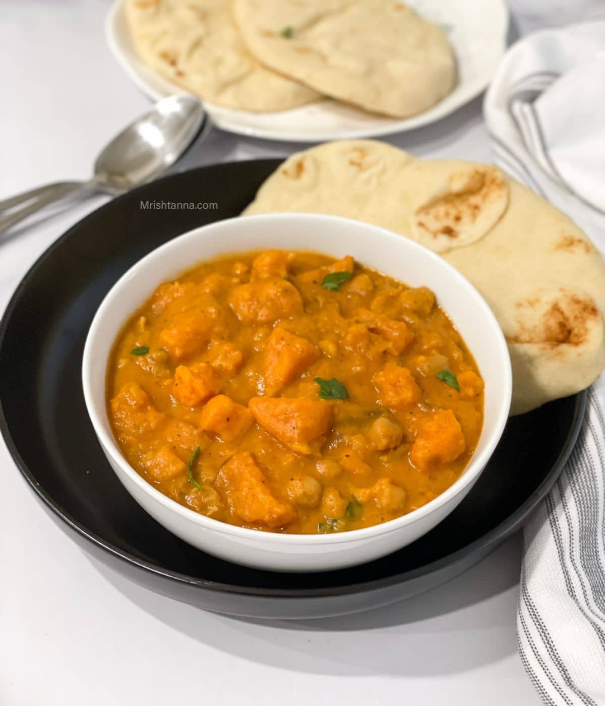 A bowl of sweet potato curry is on the plate with vegan naan.