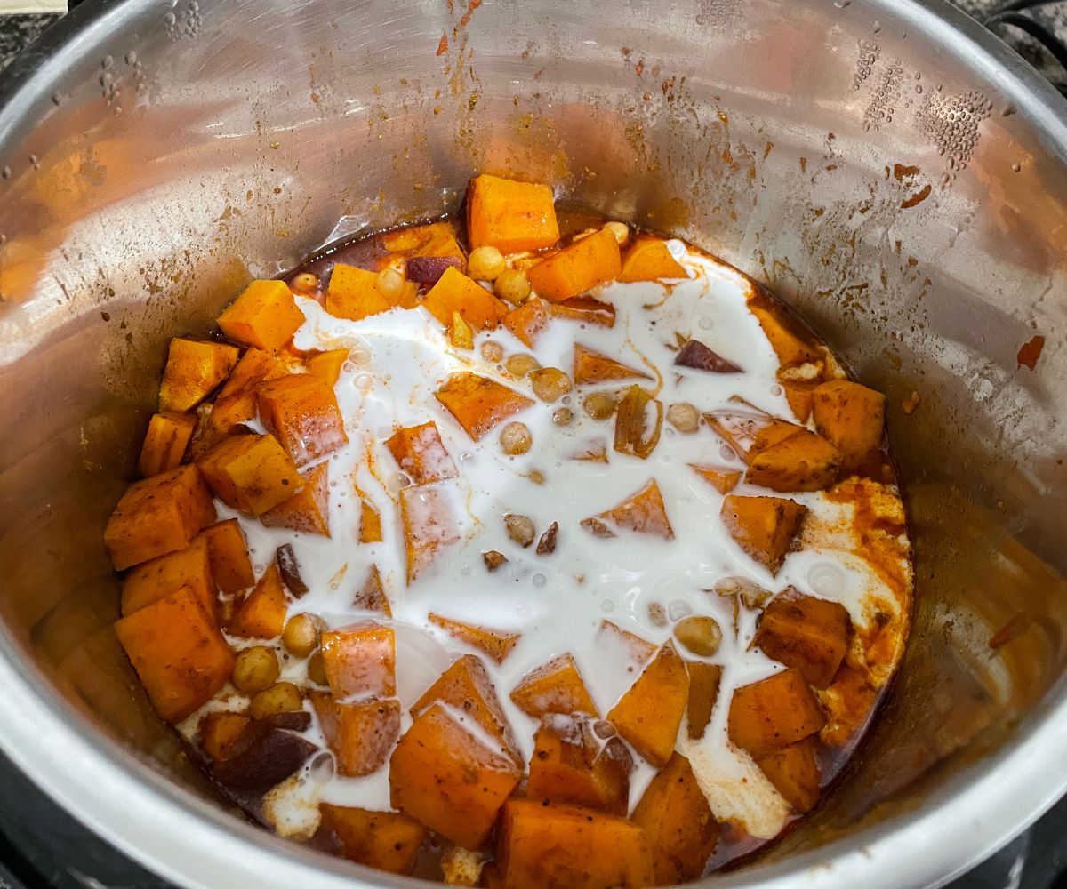 An instant pot is with sweet potato curry and topped with coconut milk.
