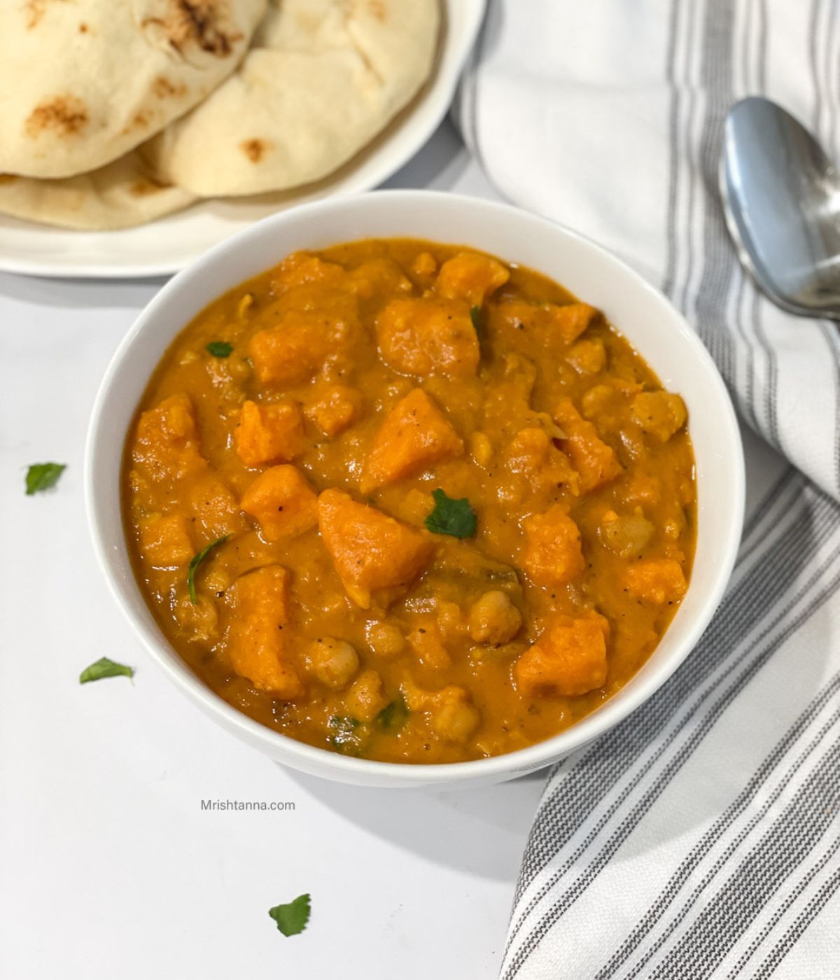 A bowl of Instant pot sweet potato curry is on the table along with a plate of naan.