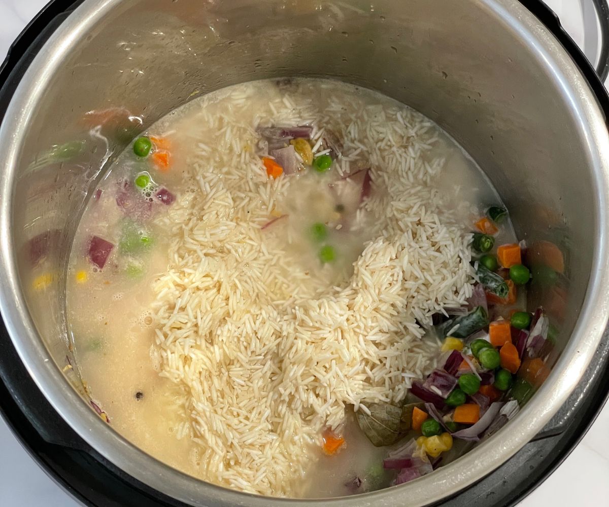 A pot is with uncooked vegetable pulao mixture.