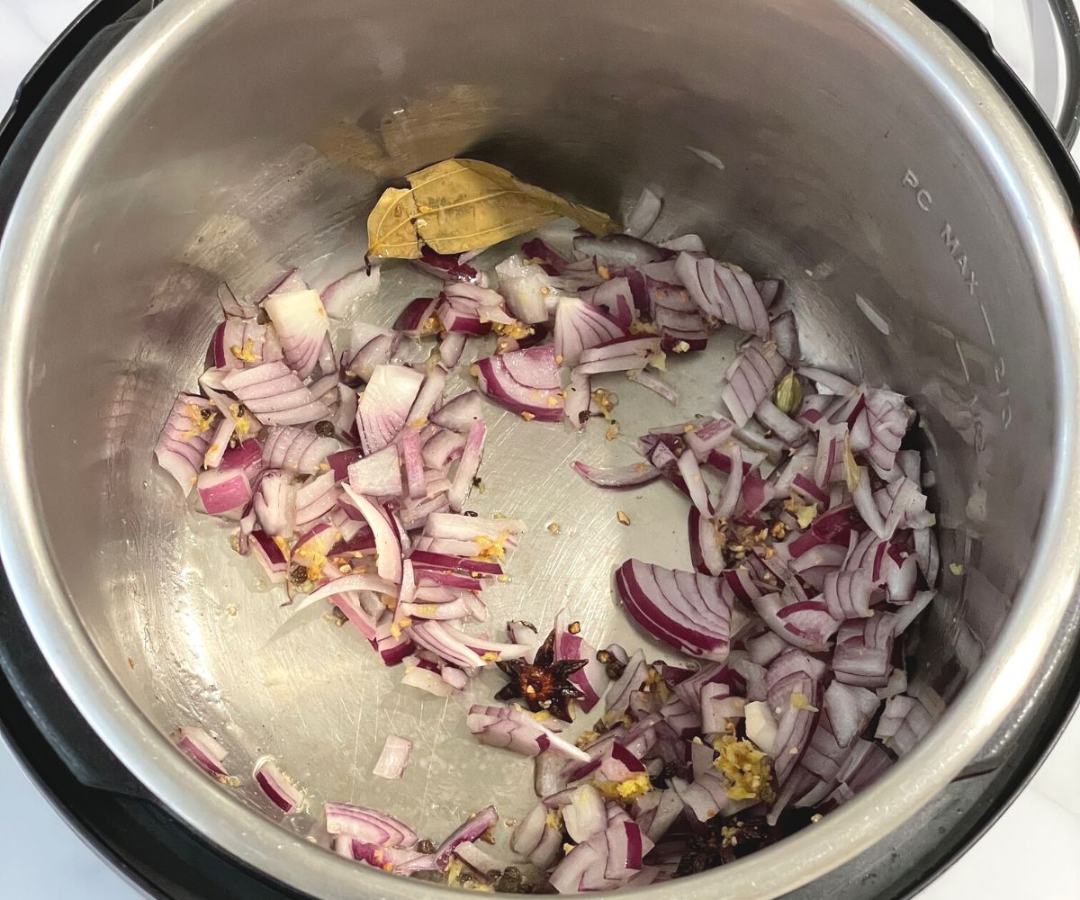 An instant pot is with whole spices, and chopped onions on the saute mode.