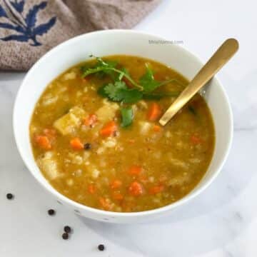 A white bowl of mulligatawny soup is with a golden spoon.