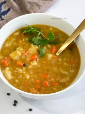 A white bowl of mulligatawny soup is with a golden spoon.