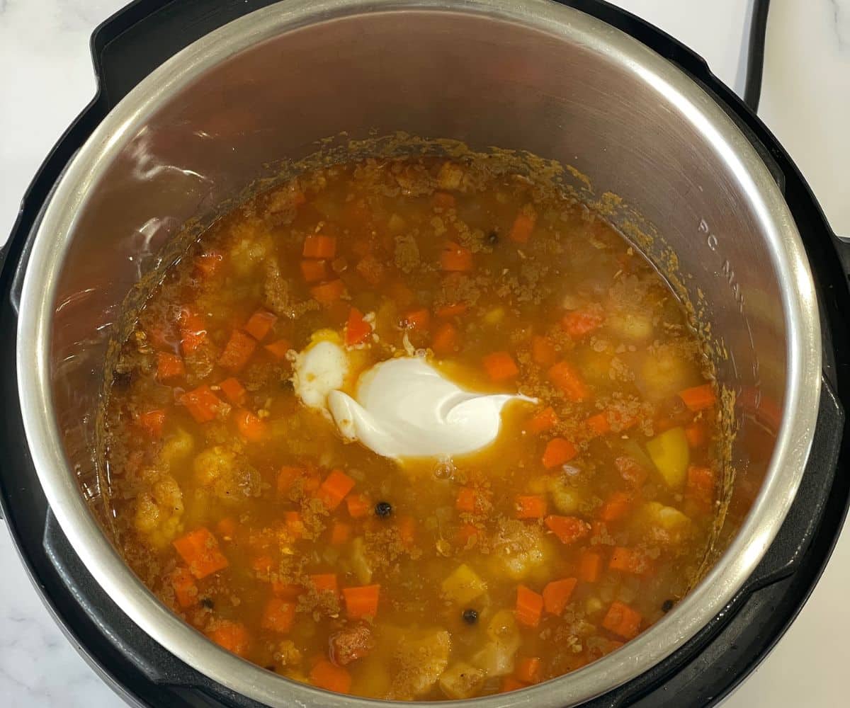 An instant pot is with mulligatawny soup and coconut milk.