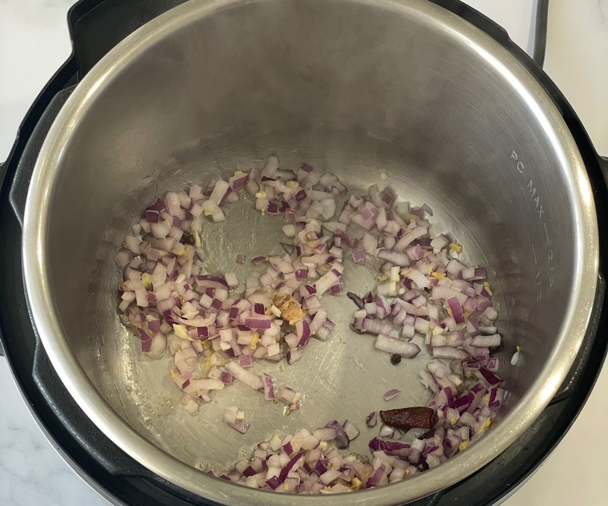 An instant pot is with oil, and chopped onions on saute mode.