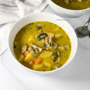 A white bowl of mushroom potato soup is on the table with a spoon by the side.