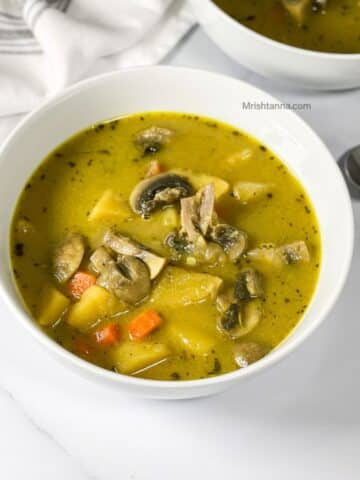 A white bowl of mushroom potato soup is on the table with a spoon by the side.