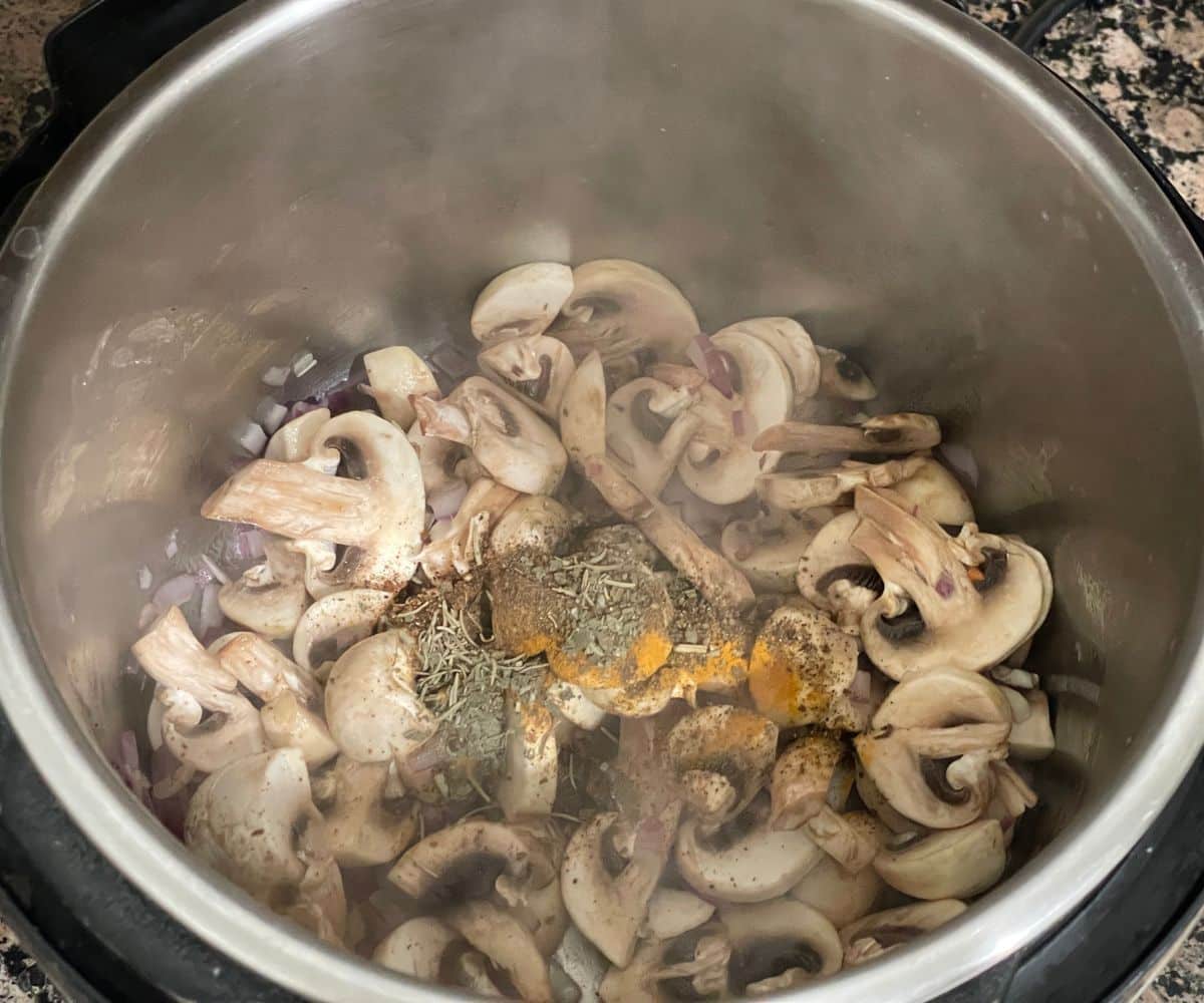 An instant pot is with chopped mushrooms and dried herbs and spice powders on saute mode.