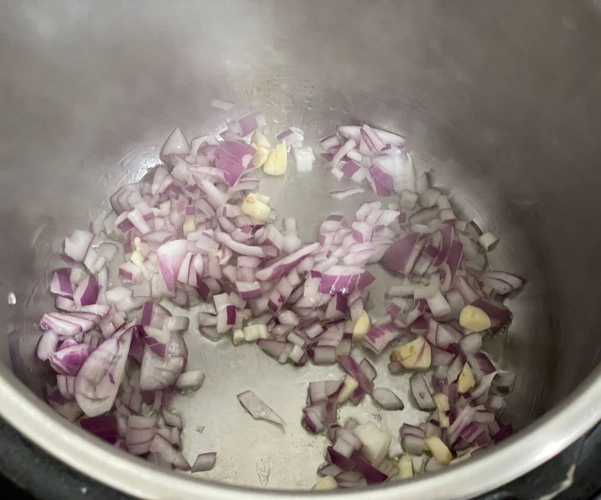 An instant pot is with chopped onions and garlic.